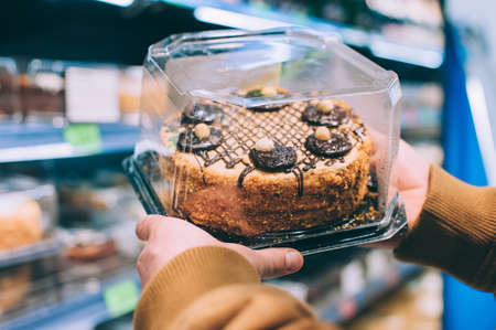 A shopper in a supermarket holds a box with a cakeの写真素材