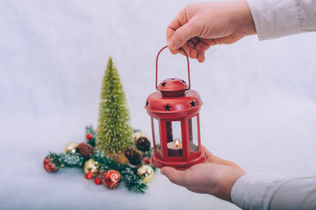 The guy holds a lamp with candles in his hands on the background of a Christmas compositionの写真素材