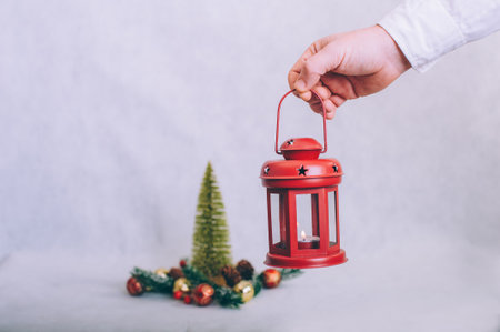 The guy holds a lamp with candles in his hands on the background of a Christmas compositionの写真素材
