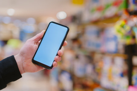 Mock-up technology. The guy holds a smartphone in his hands on the background supermarketの写真素材