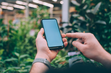 Mock-up technology. The guy holds a smartphone in his hands on the background flowersの写真素材
