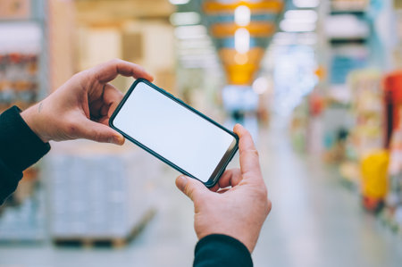 Mock-up technology. The guy holds a smartphone in his hands on the background supermarketの写真素材