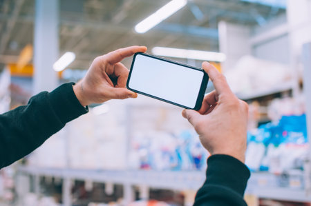Mock-up technology. The guy holds a smartphone in his hands on the background supermarketの写真素材