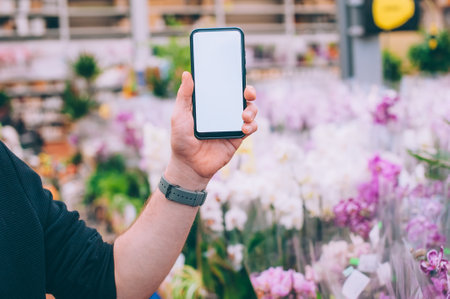 Mock-up technology. The guy holds a smartphone in his hands on the background flowersの写真素材