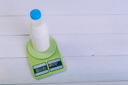A bottle of milk on a kitchen scale on a wooden tableの写真素材