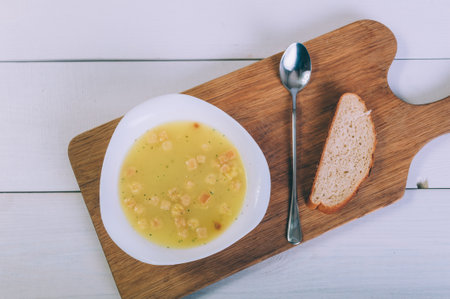 Soup broth in a bowl with bread on a wooden tableの写真素材