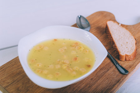 Soup broth in a bowl with bread on a wooden tableの写真素材