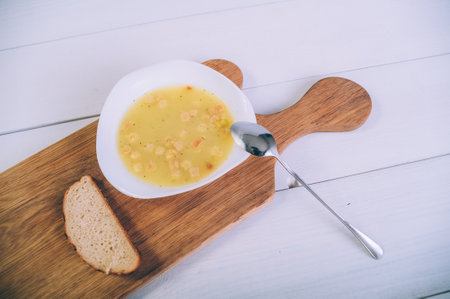 Soup broth in a bowl with bread on a wooden tableの写真素材