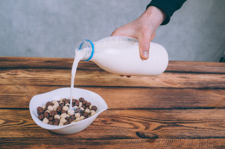 A man pours milk into cornflakes on a wooden backgroundの写真素材