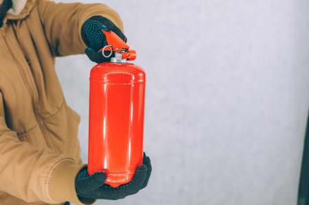 A man holds a red fire extinguisher in his hands on a white backgroundの写真素材