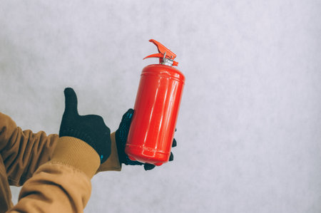 A man holds a red fire extinguisher in his hands on a white backgroundの写真素材