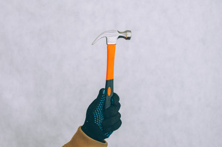A man holds a construction hammer in his hands on a light backgroundの写真素材