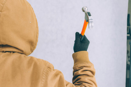 A man holds a construction hammer in his hands on a light backgroundの写真素材