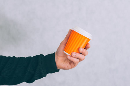A man holds a mock-up of a paper cup for coffee and tea on a light backgroundの写真素材