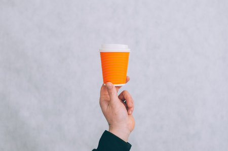 A man holds a mock-up of a paper cup for coffee and tea on a light backgroundの写真素材