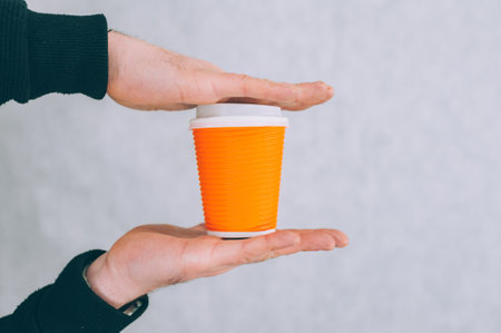 A man holds a mock-up of a paper cup for coffee and tea on a light backgroundの写真素材