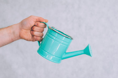 A man holds a garden watering can in his hands on a light backgroundの写真素材
