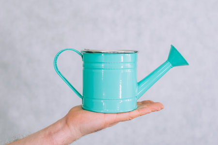 A man holds a garden watering can in his hands on a light backgroundの写真素材