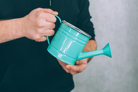 A man holds a garden watering can in his hands on a light backgroundの写真素材