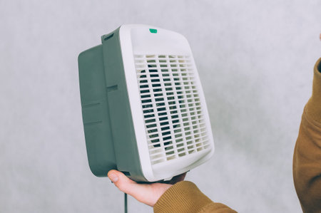 A man holds a heater in his hands on a light backgroundの写真素材