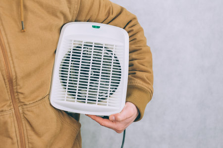 A man holds a heater in his hands on a light backgroundの写真素材