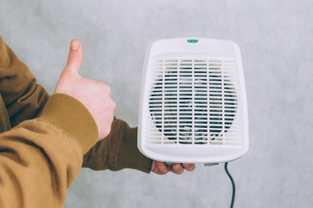 A man holds a heater in his hands on a light backgroundの写真素材