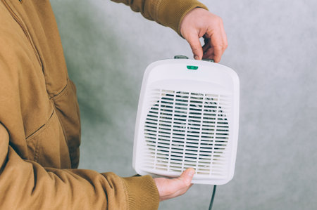 A man holds a heater in his hands on a light backgroundの写真素材