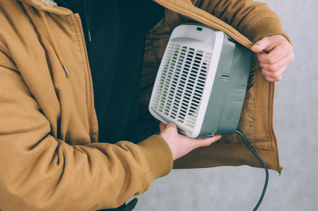 A man holds a heater in his hands on a light backgroundの写真素材
