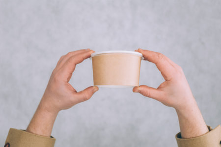 A man holds a mock-up of a paper cup for soup, coffee and tea on a light backgroundの写真素材