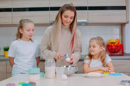 Mom teaches her daughters to cook dough in the kitchenの写真素材