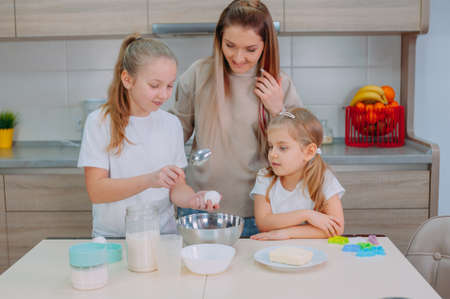 Mom teaches her daughters to cook dough in the kitchenの写真素材