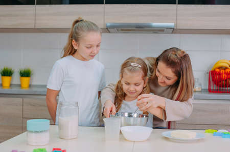 Mom teaches her daughters to cook dough in the kitchenの写真素材