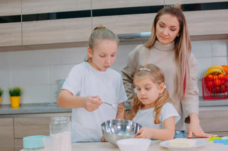 Mom teaches her daughters to cook dough in the kitchenの写真素材