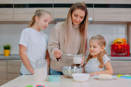 Mom teaches her daughters to cook dough in the kitchenの写真素材