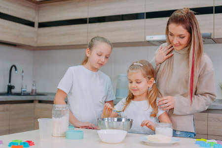 Mom teaches her daughters to cook dough in the kitchenの写真素材
