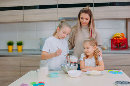 Mom teaches her daughters to cook dough in the kitchenの写真素材