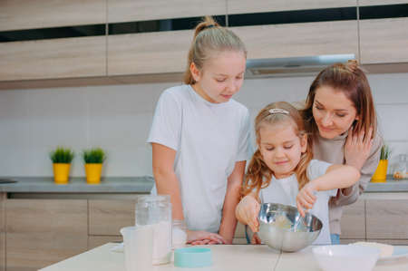 Mom teaches her daughters to cook dough in the kitchenの写真素材
