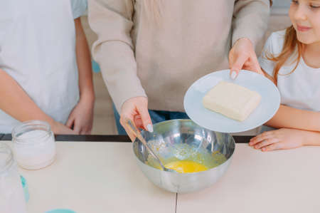Mom teaches her daughters to make dough in the kitchen and beat eggsの写真素材