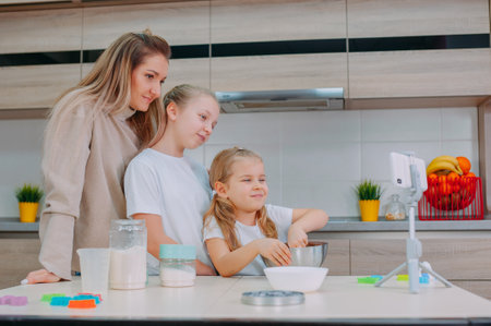 Mom teaches her daughters to cook dough in the kitchen. The family is filming a culinary video on a smartphoneの写真素材
