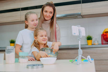 Mom teaches her daughters to cook dough in the kitchen. The family is filming a culinary video on a smartphoneの写真素材