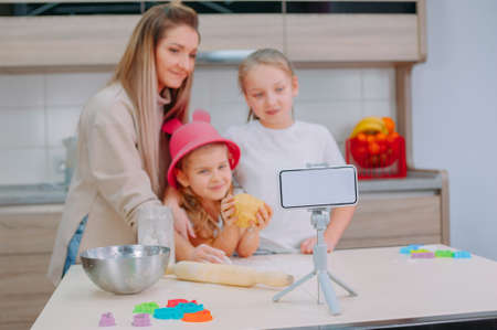 Mom teaches her daughters to cook dough in the kitchen. The family is filming a culinary video on a smartphoneの写真素材