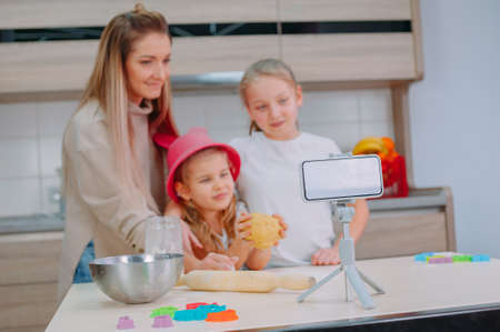 Mom teaches her daughters to cook dough in the kitchen. The family is filming a culinary video on a smartphoneの写真素材