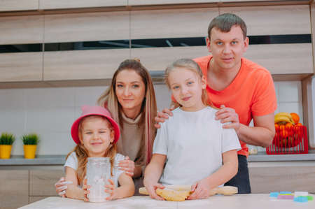 Mom with Father teaches two daughters to cook dough in the kitchenの写真素材