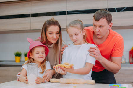Mom with Father teaches two daughters to cook dough in the kitchenの写真素材