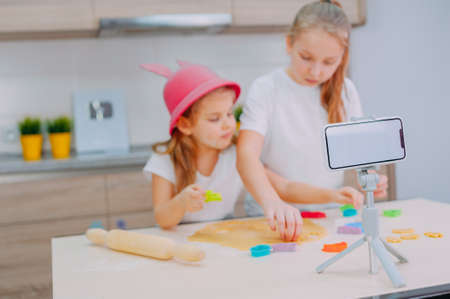 Two sisters bloggers are preparing cookies in the kitchen and filming a culinary video on a smartphoneの写真素材
