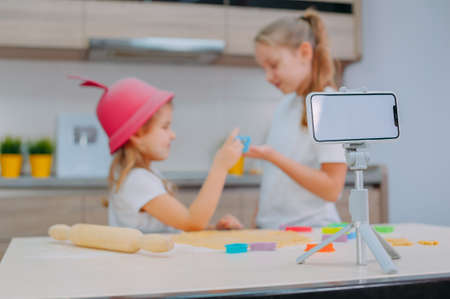 Two sisters bloggers are preparing cookies in the kitchen and filming a culinary video on a smartphoneの写真素材
