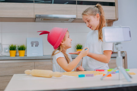 Two sisters bloggers are preparing cookies in the kitchen and filming a culinary video on a smartphoneの写真素材