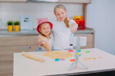 Two sisters bloggers are preparing cookies in the kitchen and filming a culinary video on a smartphoneの写真素材