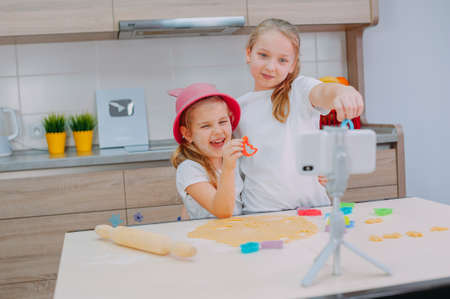 Two sisters bloggers are preparing cookies in the kitchen and filming a culinary video on a smartphoneの写真素材