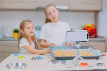 Two sisters bloggers are making cookies and filming training videos on a smartphoneの写真素材